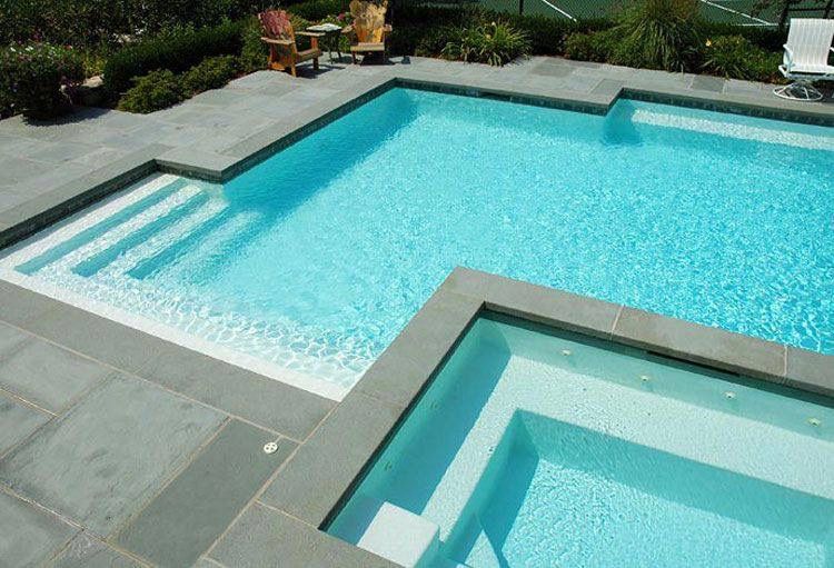 Piscina sobre suelo con dos espacios diferenciados, plaqueta gris alrededor y escaleras de obra, rodeada de jardín